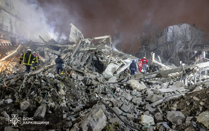 Emergency responders in protective gear clearing debris from a destroyed building in Ukraine following a drone attack.